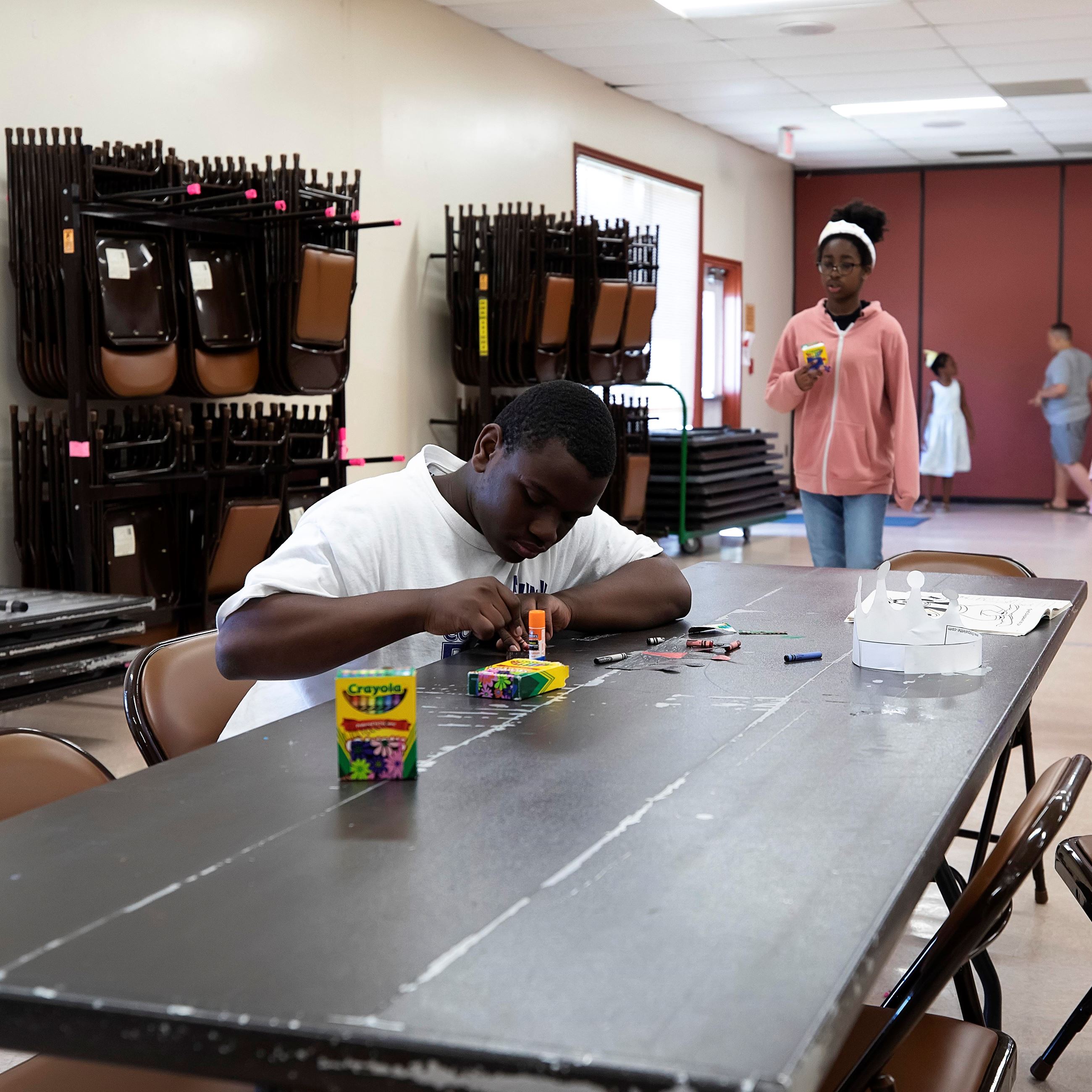 Child sitting at a table coloring with chairs hanging in the background