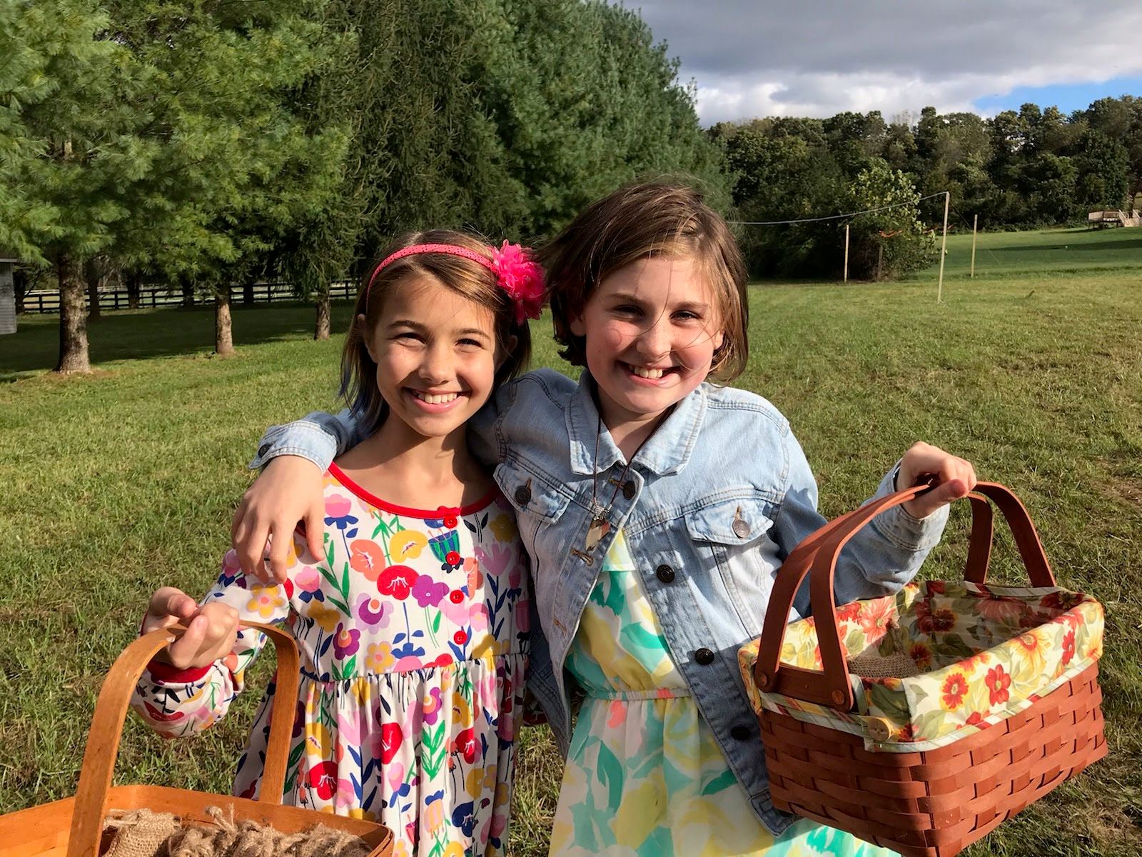 Two girls in the park smiling and holding picnic baskets